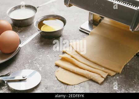 Pasta-Maschine mit Teig und Zutaten auf grauem Hintergrund Stockfoto