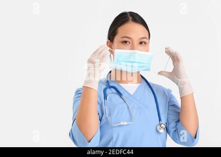 Portrait der weiblichen asiatischen Arzt setzen auf medizinische Maske gegen Heller Hintergrund Stockfoto