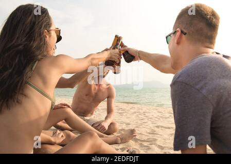 Gruppe von Freunden mit Party claging Bierflaschen machen ein Toasten Sie, bevor Sie im Sommer am Strand trinken Stockfoto