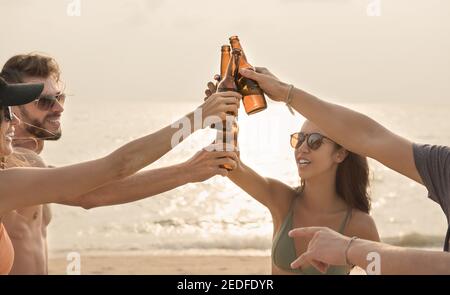 Gruppe von Freunden mit Feier Party Klaging Bierflaschen machen Ein Toast vor dem Trinken am Strand in der Dämmerung Stockfoto