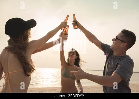 Gruppe von Freunden mit Feier Party Klaging Bierflaschen machen Ein Toast vor dem Trinken am Strand in der Dämmerung Stockfoto