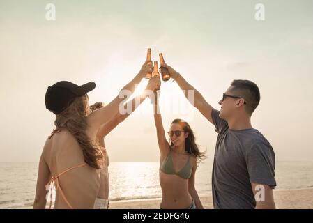 Gruppe von Freunden klatschen Bierflaschen mit Feier Party und Trinken am Strand im Sommer Stockfoto