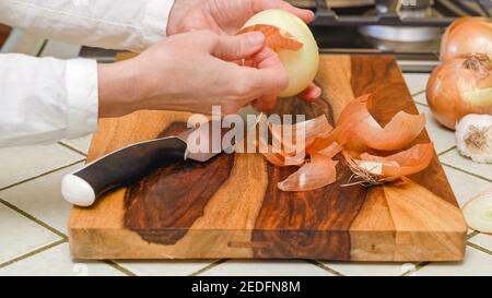 Kaukasische Frau Hände schälende Zwiebel auf Holzbrett auf Küchenarbeitsplatten, Nahaufnahme, Lebensstil Stockfoto