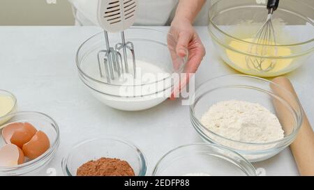 Schokoladenkuchen Schritt für Schritt Rezept. Frau Hände schlagen Eiweiß mit Mixer. Nahaufnahme des Vorbereitungsprozesses Stockfoto