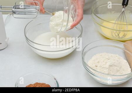 Nahaufnahme Backvorgang. Der Küchenchef fügt Sauerrahm in eine Schüssel mit geschältem Eiweiß. Stockfoto