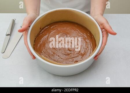 Kuchenform mit Kuchenteig close up auf Küchentisch, close up Backprozess. Schokoladenkuchen Schritt für Schritt Rezept, Frau Hände Stockfoto