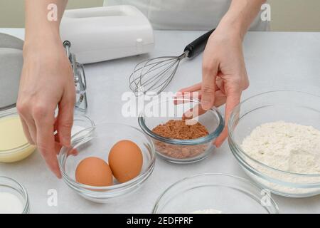 Zutaten und Gerichte für die Herstellung von Schokoladenkuchen aus nächster Nähe auf Küchentisch. Schritt für Schritt Schokoladenkuchen Rezept, Frau Hände Stockfoto
