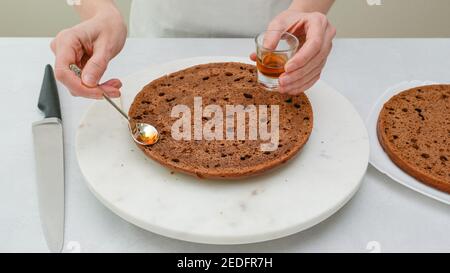 Frau Hände Gießen Rum Sauce über Schokoladenkuchen. Schritt für Schritt Schokoladenkuchen Rezept, close up Backprozess, Teil der Serie Stockfoto