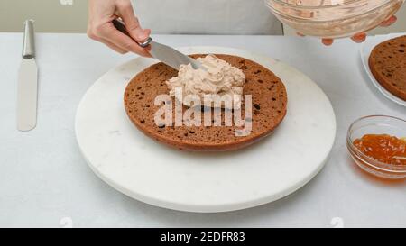 Zusammenbauen des Schokoladenkuchens. Koch platziert Schokoladenkuchen Zuckerguss auf der ersten Schicht. Schritt für Schritt Schokoladenkuchen Rezept Stockfoto