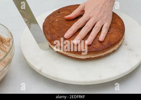 Zusammenbauen des Schokoladenkuchens. Schritt für Schritt Schokoladenkuchen mit Schokoladencreme Rezept, close up Backprozess, Frau Hände Stockfoto