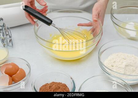 Schokoladenkuchen Schritt für Schritt Rezept. Frau Whisks Eigelb mit Zucker in einer Glasschüssel, close up Zubereitungsvorgang Stockfoto