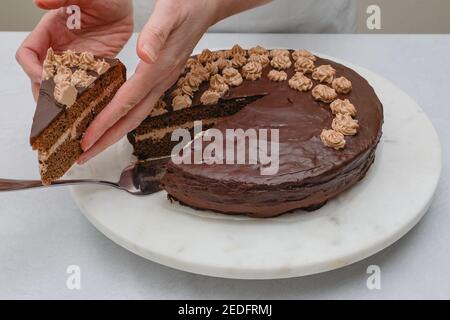 Schokoladenkuchen mit Schokoladencreme und Schokoladenganache aus nächster Nähe. Frau Hände servieren Kuchen, Nahaufnahme Stockfoto
