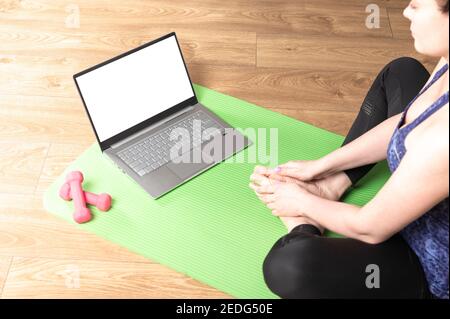 Frau praktiziert einige Meditation und Yoga zu Hause in einem Laptop-Computer mit Mockup weißen leeren Bildschirm Stockfoto