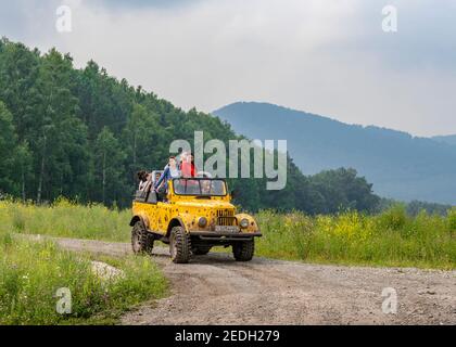 MOUNTAIN ALTAI, RUSSLAND - 27. JULI 2019: Eine Gruppe von jungen Menschen, die den Berg in einem gelben Auto mit einem offenen Gipfel Stockfoto