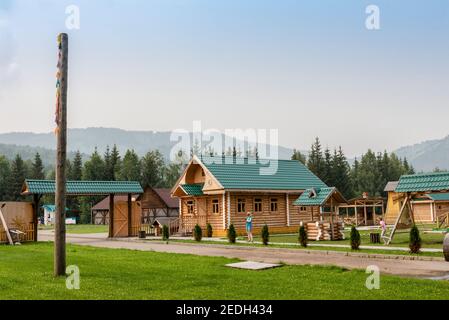 BERG ALTAI, RUSSLAND - 27. JULI 2019: Traditionelle russische Dorfhof mit breiten Toren unter dem Dach, Holzhütte und Brunnen im Altai Mountai Stockfoto