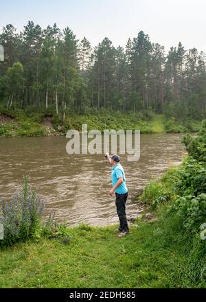 MOUNTAIN ALTAI, RUSSLAND - 27. JULI 2019: Ein Mann, der im Fluss Katun gegen den Wald fischt Stockfoto