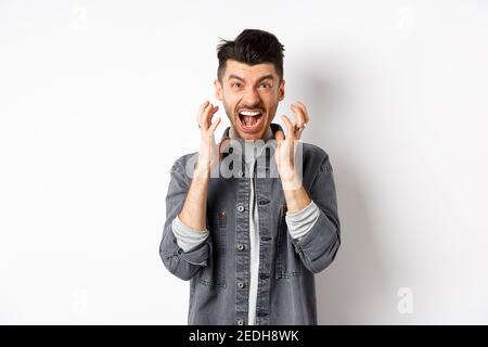 Wütender Mann schreiend bekümmert, Temperament verlierend und frustriert schreiend, starrend auf etwas Schlechtes, stehend auf weißem Hintergrund Stockfoto