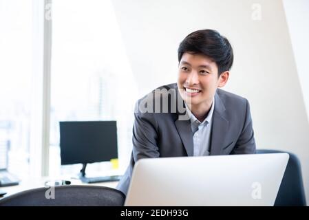 Junger lächelnder asiatischer chinesischer Geschäftsmann, der im Büro arbeitet Stockfoto