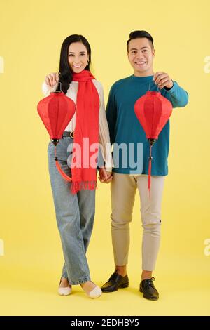 Ziemlich junge asiatische Freund und Freundin in warmen Pullover halten Hände und Seidenlaternen Stockfoto