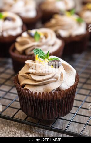 Hausgemachte Schokoladen-Cupcakes mit Tiramisu-Sahne, Schokoladenkaffeebohnen und Minze. Selektiver Fokus. Stockfoto