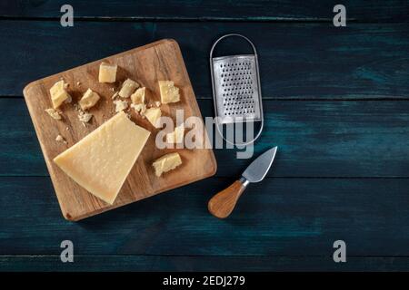 Zerbröckelter Parmesankäse mit einem Messer und einer Reibe, von oben auf einem dunklen Holzhintergrund mit einem Platz für Text geschossen Stockfoto