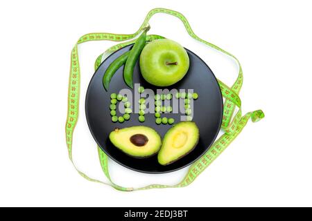 Kreative flache Lay-Komposition aus einem ganzen grünen Apfel, Schnitt Avocado und weiches Maßband auf einem schwarzen Teller mit einem Wort ERNÄHRUNG aus frischen Gartenerbsen Stockfoto