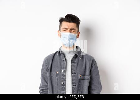 Konzept für Gesundheit, Gesundheit und Pandemie. Trauriger weinender Mann in medizinischer Maske, der sich über Quarantäne aufregt, auf weißem Hintergrund stehend Stockfoto
