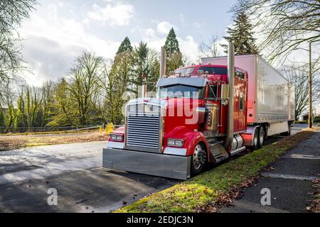 Beliebte leistungsstarke Haube rot klassischen amerikanischen Idol großen Rig semi LKW mit glänzenden Chromteilen und weiß bedecktem Trockenvan Sattelauflieger auf der Stadt geparkt Stockfoto