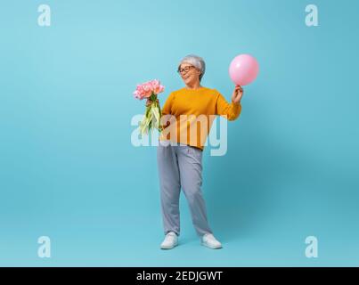 Schöne ältere Frau mit rosa Blumen Tulpen in den Händen auf Farbe blauen Hintergrund. Stockfoto