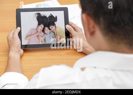 Geschäftsmann sprechen mit Familie auf Tablet über Internet-Videokonferenz im Büro. Covid-19, Coronavirus Ausbruch Mann sprechen mit seiner Familie durch Tablette. Stockfoto