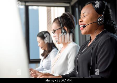 Freundliche schwarze Frau mit Mikrofon-Headset im Callcenter Mit internationalem Team als Telemarketing-Kundendienstmitarbeiter Stockfoto