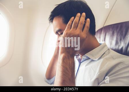 Männlicher Beifahrer mit Ohrstöpsel im Flugzeug während der Einnahme Aus (oder Landung) Stockfoto