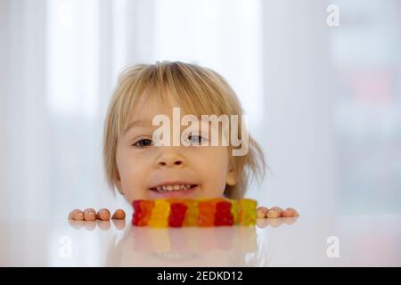 Cute Kleinkind blonde junge, Blick auf bunte Gummibärchen, sitzen auf dem Tisch Stockfoto