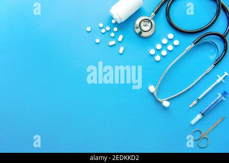 Pillen und medizinische Nachbauten einschließlich Stethoskop, Spritze und Schere am Rand auf hellblauem Hintergrund, Draufsicht mit Kopierraum Stockfoto