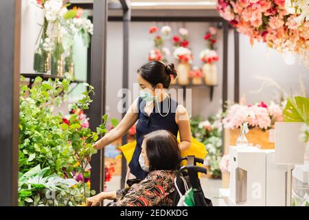 Ältere Frau mit Tochter in Schutzmaske wählt künstliche Blumenzweig im Geschäft. Stockfoto