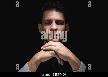 Nachdenkender Mann im schwarzen Anzug mit Händen am Kinn Dunkler Schatten starrt auf die Kamera Stockfoto