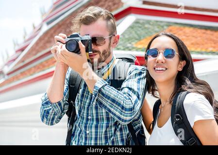 Interracial Tourist paar Rucksacktouristen, die Fotos während der Reise in Bangkok Thailand mit Thai Tempel im Hintergrund Stockfoto