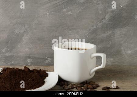 Eine Tasse Kaffee mit Kaffeebohnen und gemahlenem Kaffee auf einer Untertasse. Selektiver Fokus. Stockfoto