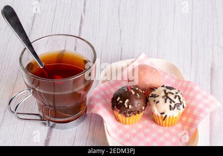 Cupcakes in verschiedenen Geschmacksrichtungen und Farben, begleitet von einer Tasse Tee Stockfoto