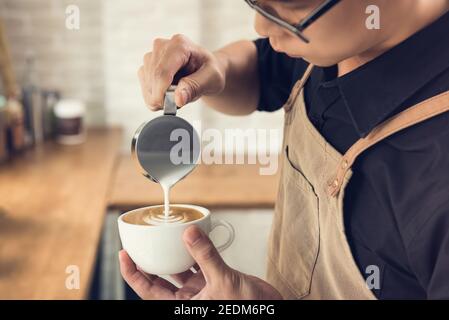 Professioneller Barista gießt gedämpfte Milch in die Kaffeetasse und macht so schön Latte Art Rosetta Muster Stockfoto