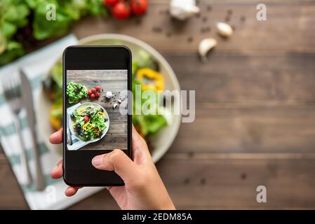 Food-Blogger mit Smartphone Foto von schönen Mix frisch Grüner Salat auf Holztisch zum Teilen in den sozialen Medien Stockfoto