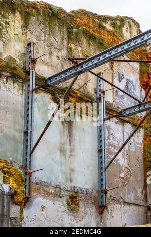 Stahlträger, die eine alte moosige Wand eines zerstörten stützen Gebäude Stockfoto