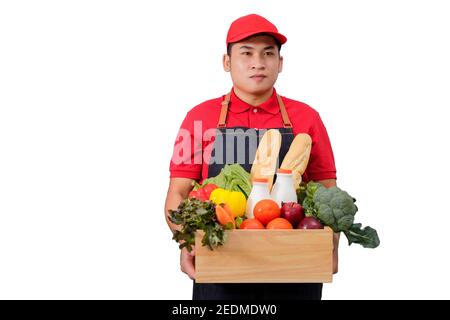 Lebensmittelgeschäft Lieferung Kurier Mann in roter Uniform mit Lebensmittelkarton mit Lebensmitteln, frischem Obst und Gemüse. Liefern Mann in roter Uniform und Schürze Handling Woode Stockfoto