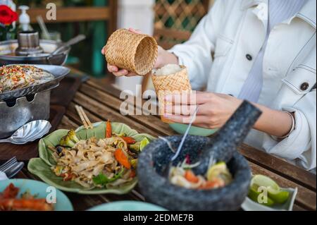 Frau öffnen klebrigen Reis Bambus-Behälter, während mit einem drei GusMenü in einem thailändischen Restaurant in der Nähe Stockfoto