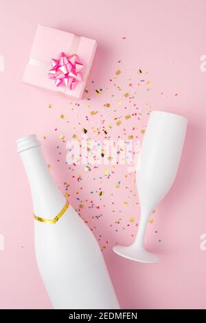 Weiße Champagner-Flasche, Geschenkbox und Champagner-Glas mit Konfetti auf rosa Hintergrund. Minimales Partykonzept. Stockfoto