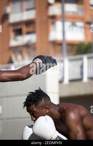 Professionelle Black Boxer trainiert Black Boxer Anfänger mit Fäustlingen und Boxhandschuhen an einem sonnigen Tag eine Outdoor Boxklasse, während sie beide schwitzen. Stockfoto