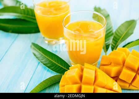 Erfrischende Getränke für den Sommer, kalter süßer und saurer exotischer Mangosaft mit Eiswürfeln in den Gläsern auf hellblauem Holztisch Stockfoto