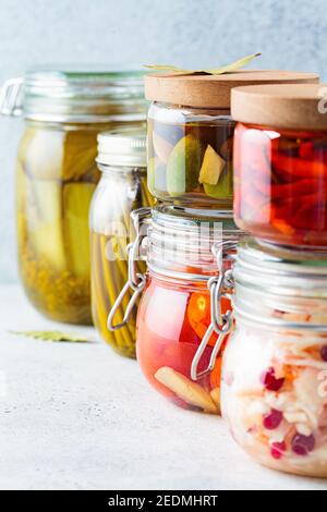 Hausgemachte eingelegte oder fermentierte Gemüse - Sauerkraut, Bärlauch, Chili, Gurken, eingelegte Tomaten und Oliven in Gläsern. Stockfoto