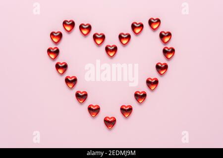 Herzform mit kleinen Glasherzen auf rosa Hintergrund. Minimales Liebeskonzept. Stockfoto