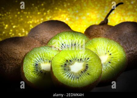 Makrofoto von lebendigen Kiwi-Scheiben auf goldenem Hintergrund.aufgenommen auf dunkler Holzplatte. Studio Foto. Stockfoto